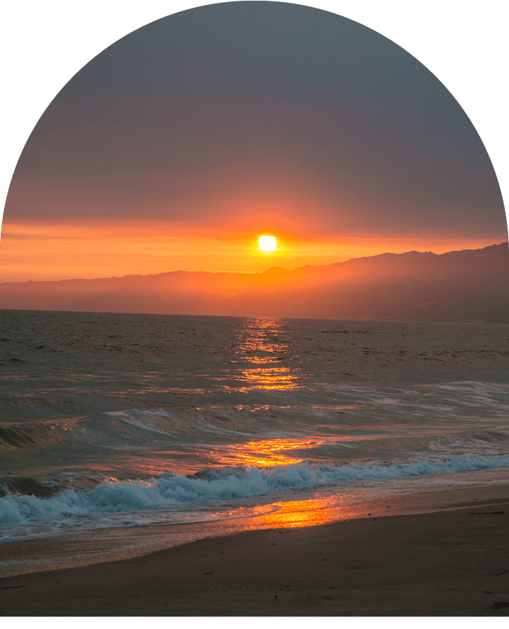 Sunset over a calm ocean with gentle waves hitting the shore.