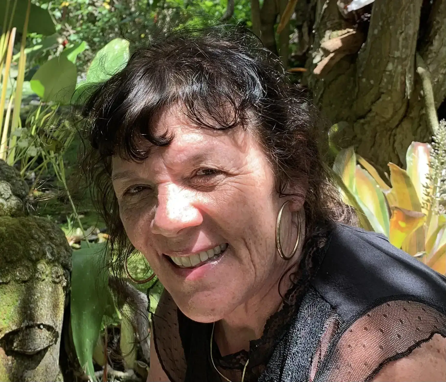 Smiling woman in outdoor natural setting with greenery.